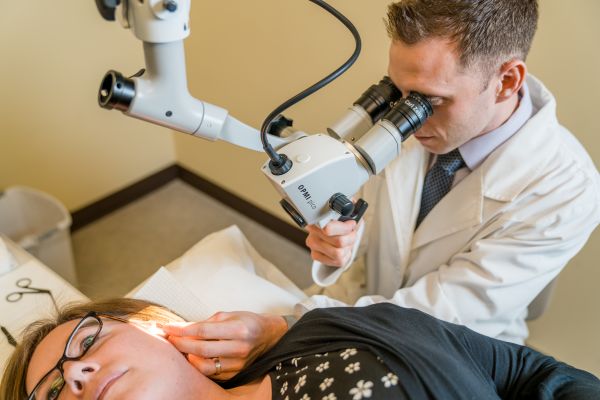White-coated medical professional performs an ear check on a female patient.