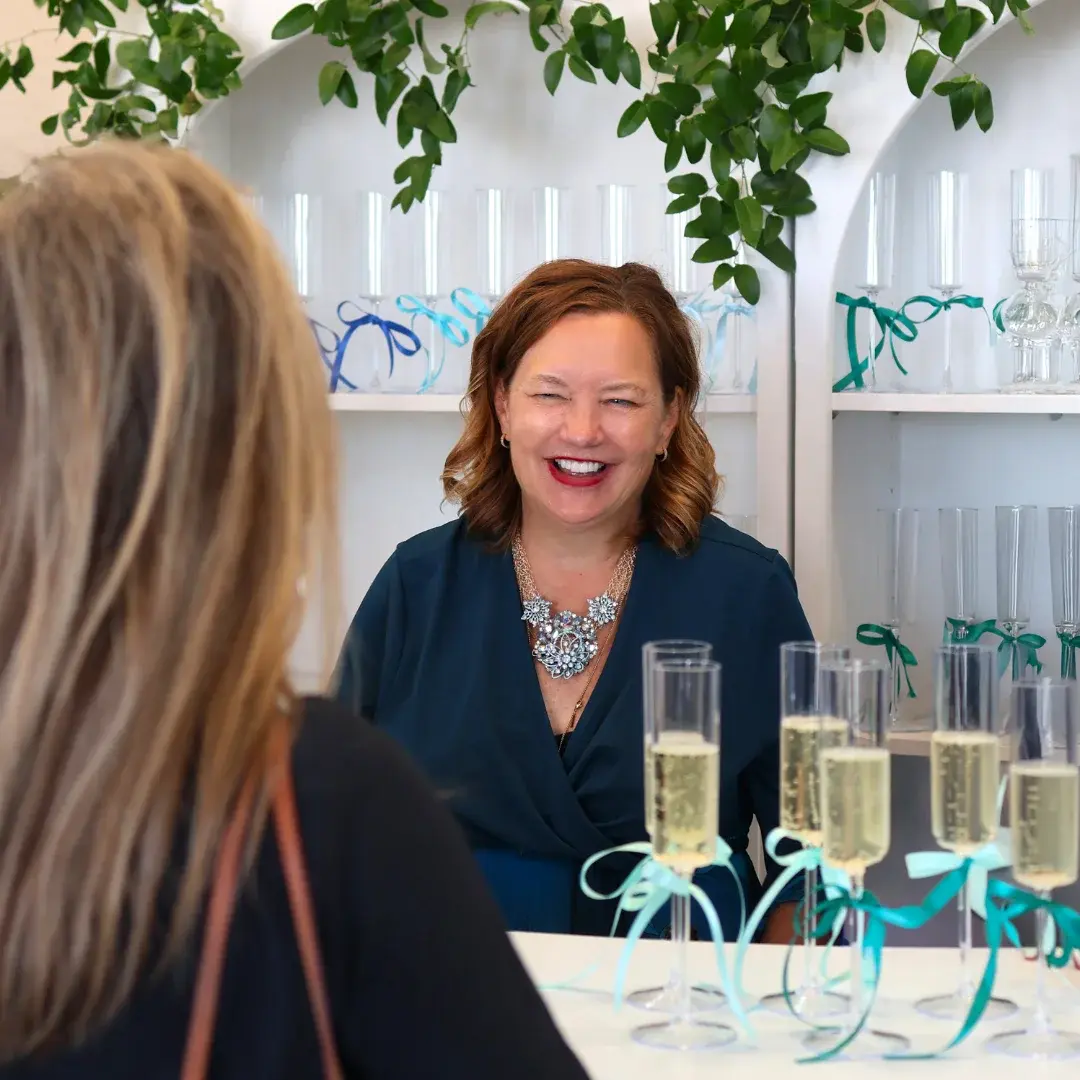 Smiling woman with red hair sits at a table with champagne glasses on it.