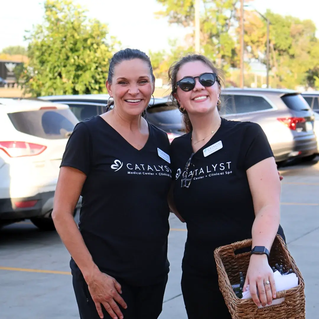 Happy coworkers with black Catalyst Medical Center + Clinical Spa shirts posing for a snapshot in a parking lot.
