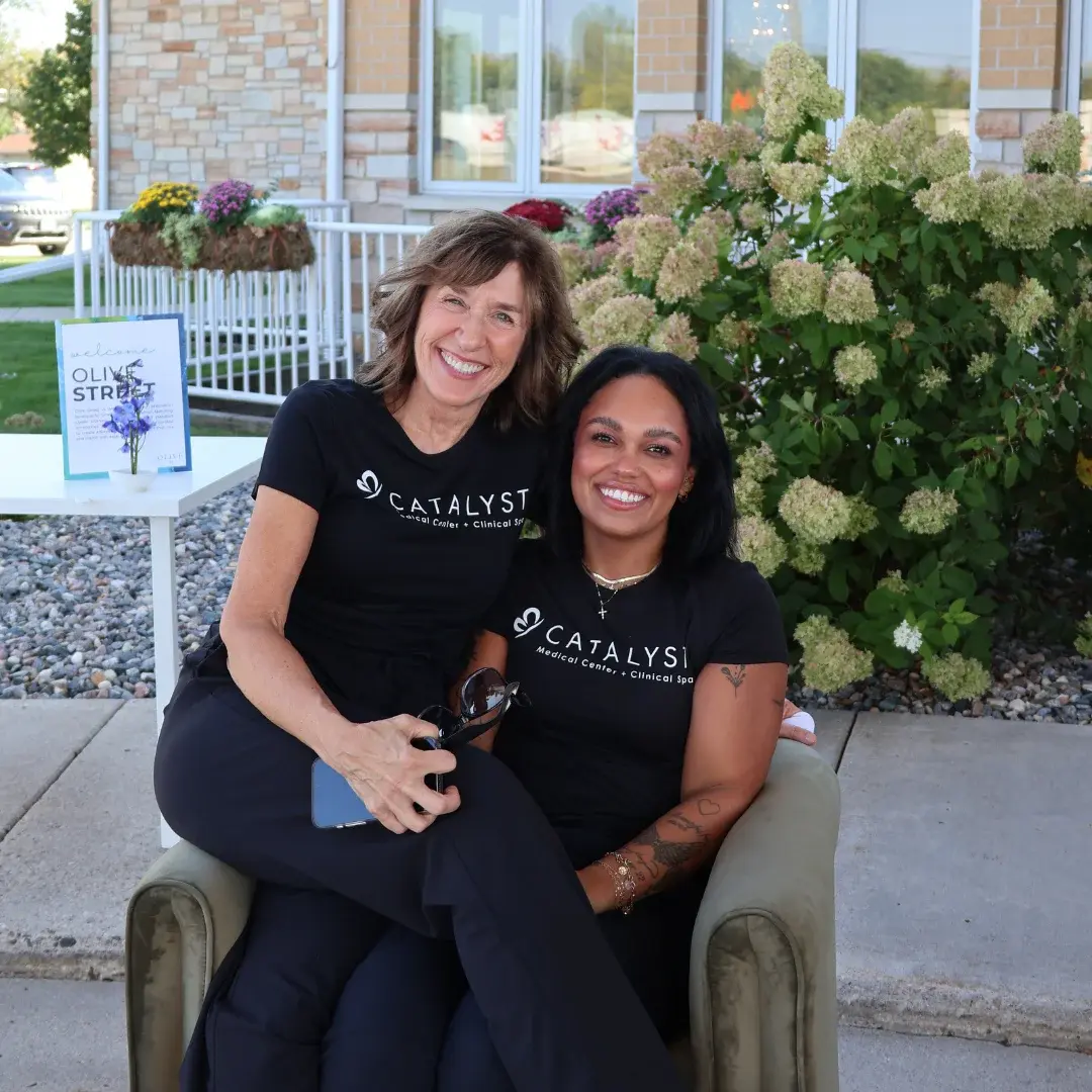 Happy coworkers with black Catalyst Medical Center + Clinical Spa shirts posing for a photo in the outdoor sitting area.