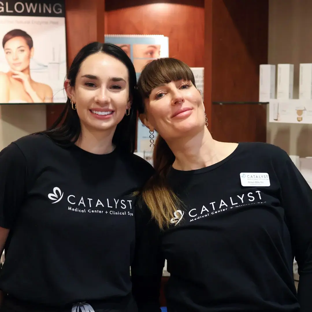 Happy coworkers with black Catalyst Medical Center + Clinical Spa shirts standing in the reception area.