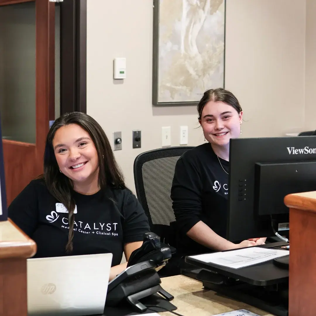 Smiling Catalyst staff sit at their desks with computer and phone equipment.